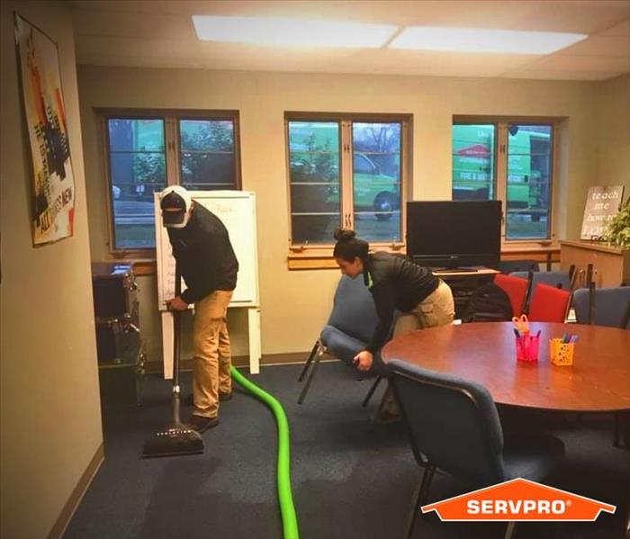 2 SERVPRO technicians extracting water from carpet with an extractor in a classroom