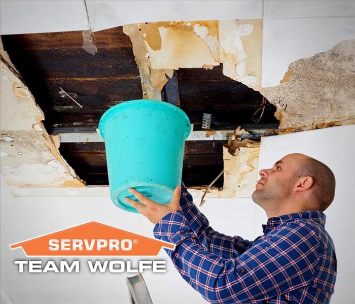 A Man using a bucket to minimize water damage from the ceiling